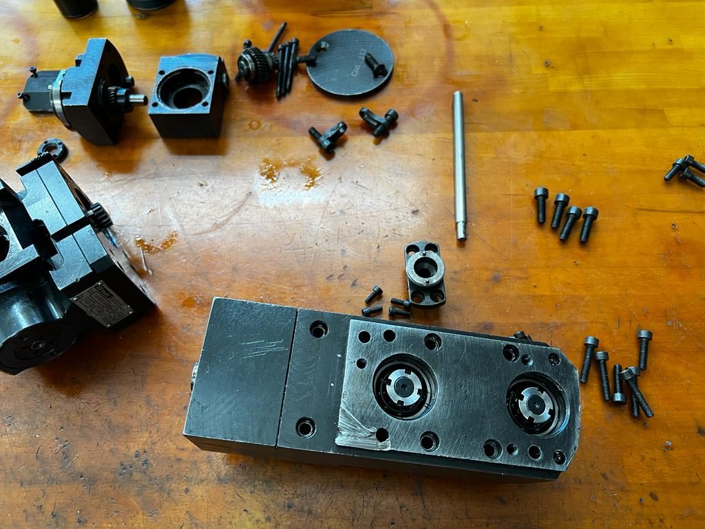 Auf einer hölzernen Werkbank lagen zerlegte, schwarze Metallmaschinenteile und Schrauben.