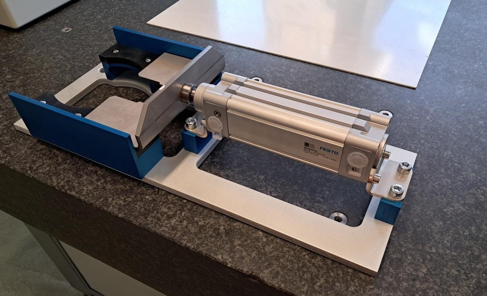 Präzisionsmechanismus in Blau und Silber auf einer Werkbank, mit transparenter zylindrischer Kammer und Metallsockel