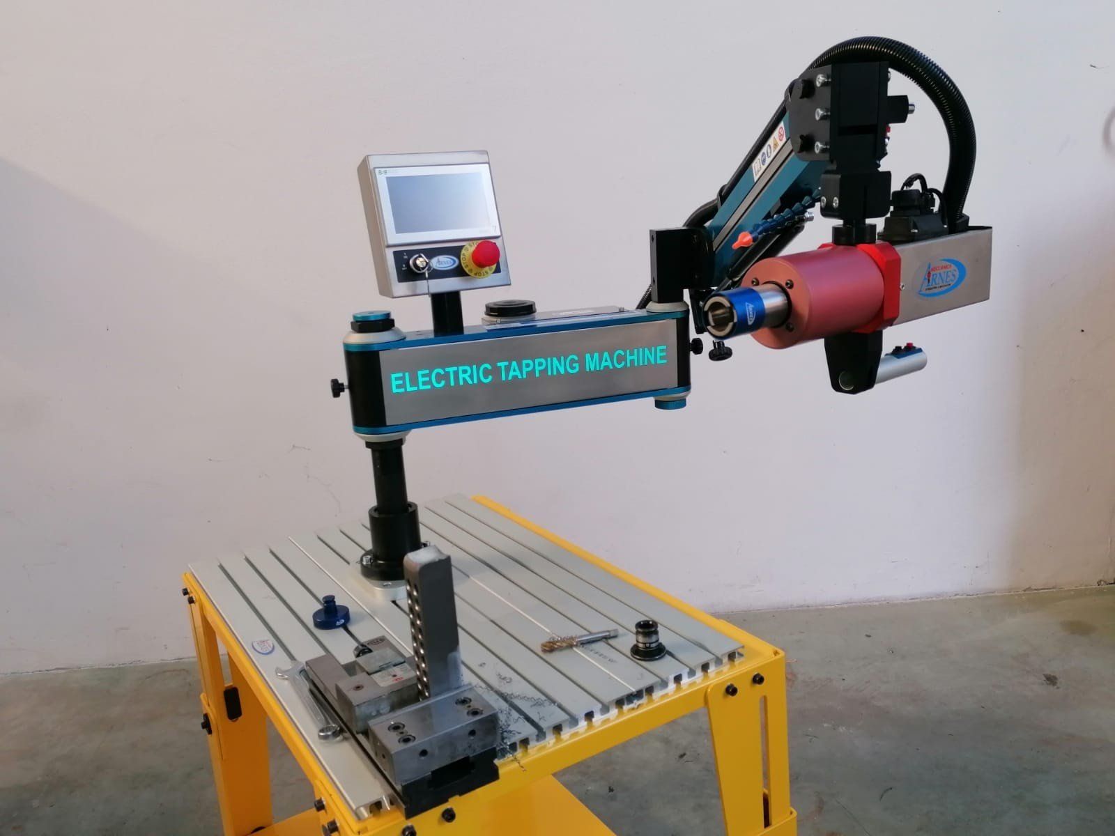 Un braccio robotico fora una piastra metallica su un banco da lavoro giallo in un'officina.