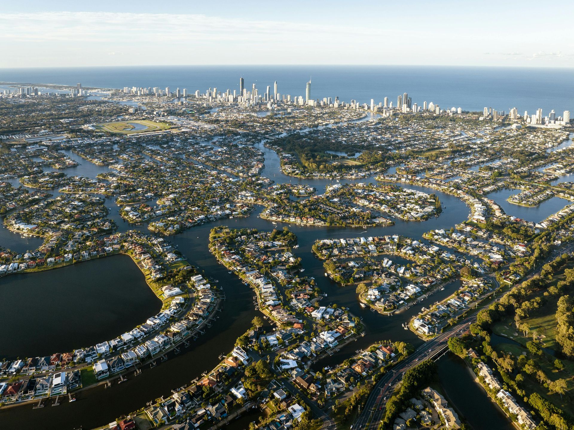 Aerial view of a coastal city featuring winding residential canals, waterways, and a high-rise skyline along the ocean.