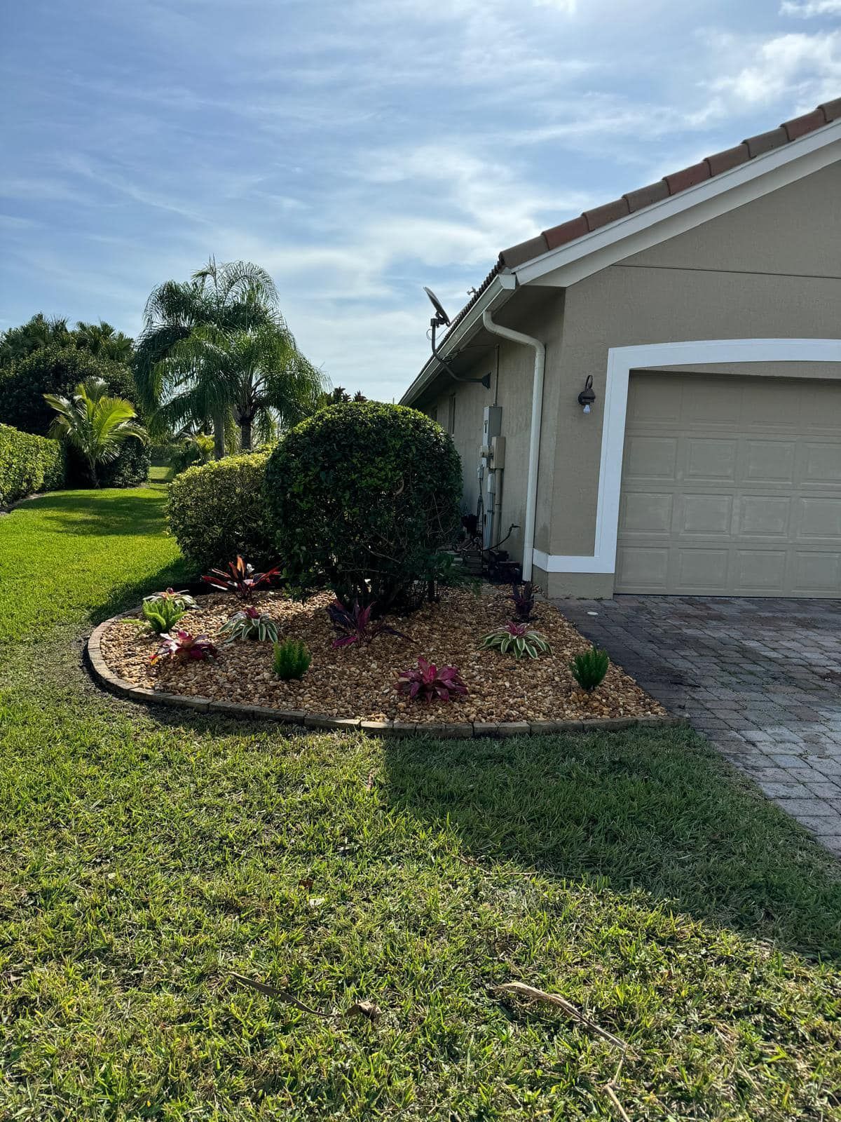 A landscaping bed with a large central shrub and small plants, mulched with rocks, next to a beige suburban garage.