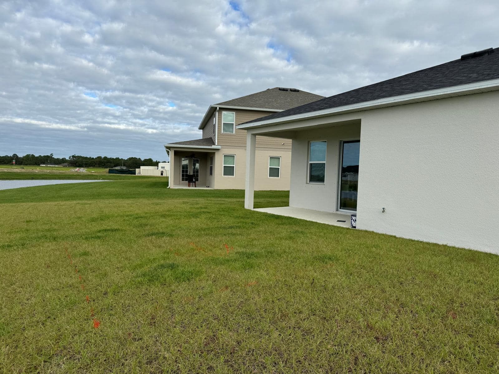 A suburban backyard overlooking a retention pond, with modern stucco houses under a cloudy sky.