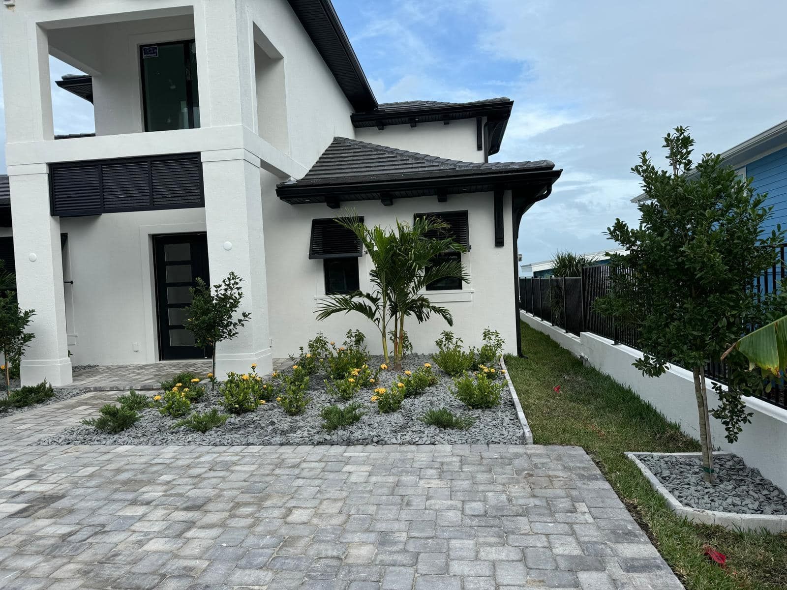 A white two-story house with a grey shingled roof, a paved driveway, and a small landscaped rock garden.