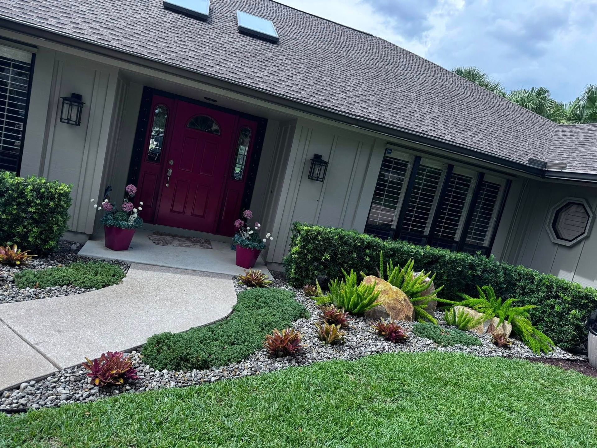 A suburban home exterior featuring a vibrant red front door, light-colored siding, and a landscaped garden bed.