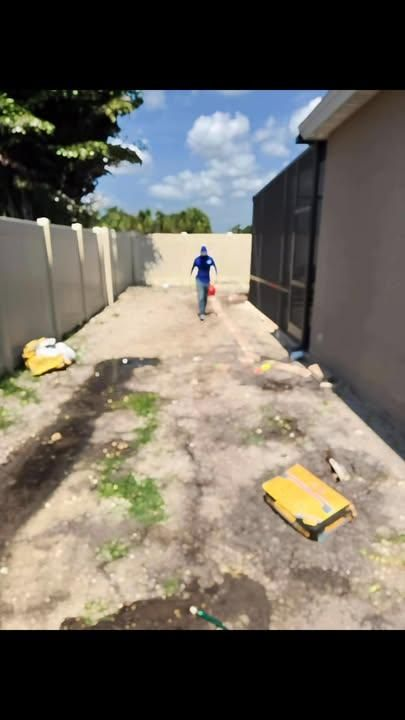 A person in a blue shirt walks down a dirt alleyway between a light-colored wall and a screened-in structure.