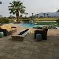 Outdoor patio with wicker furniture, a stone fire pit, and swimming pool overlooking a golf course and mountains.