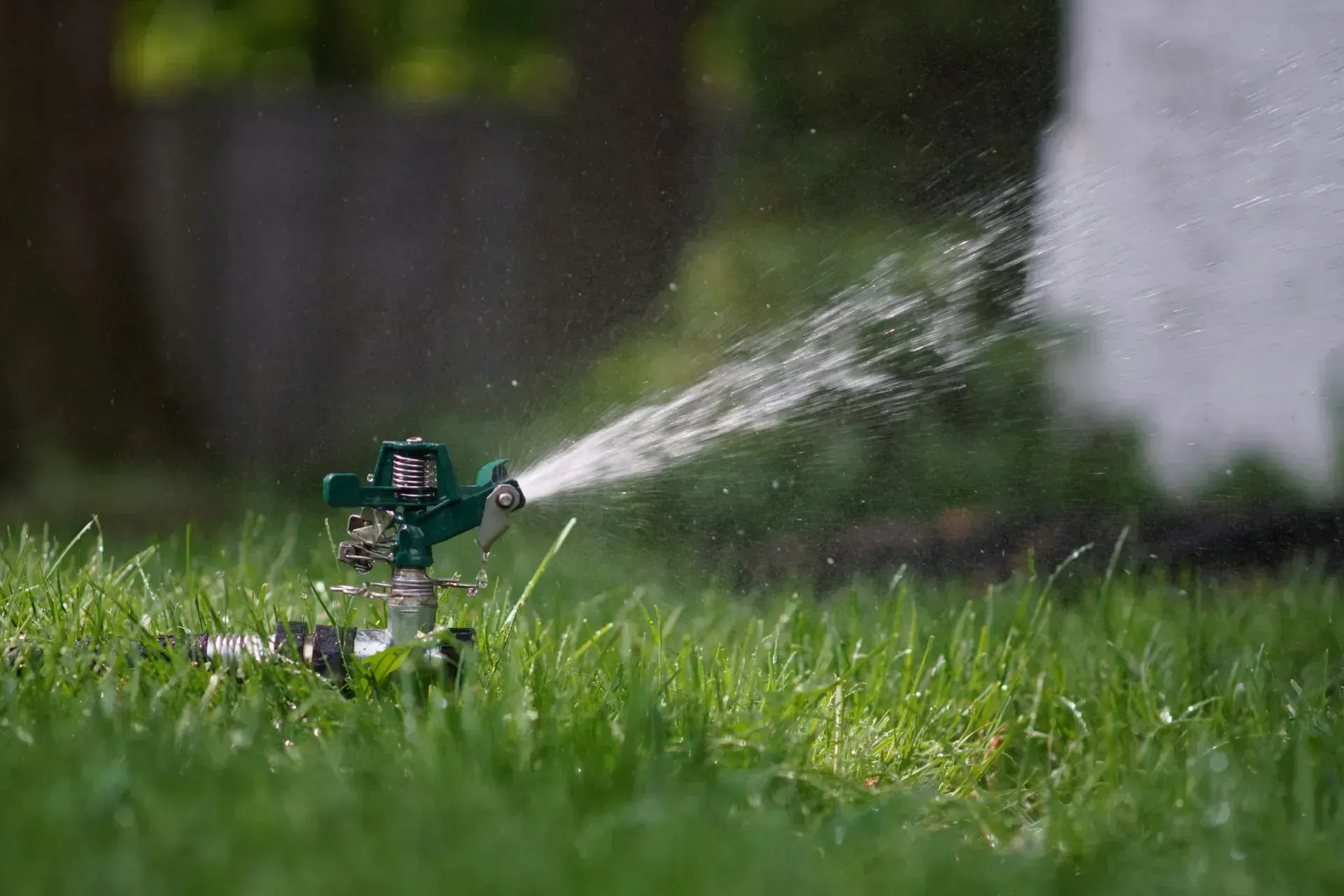 A green lawn sprinkler spraying a mist of water over a grassy yard.