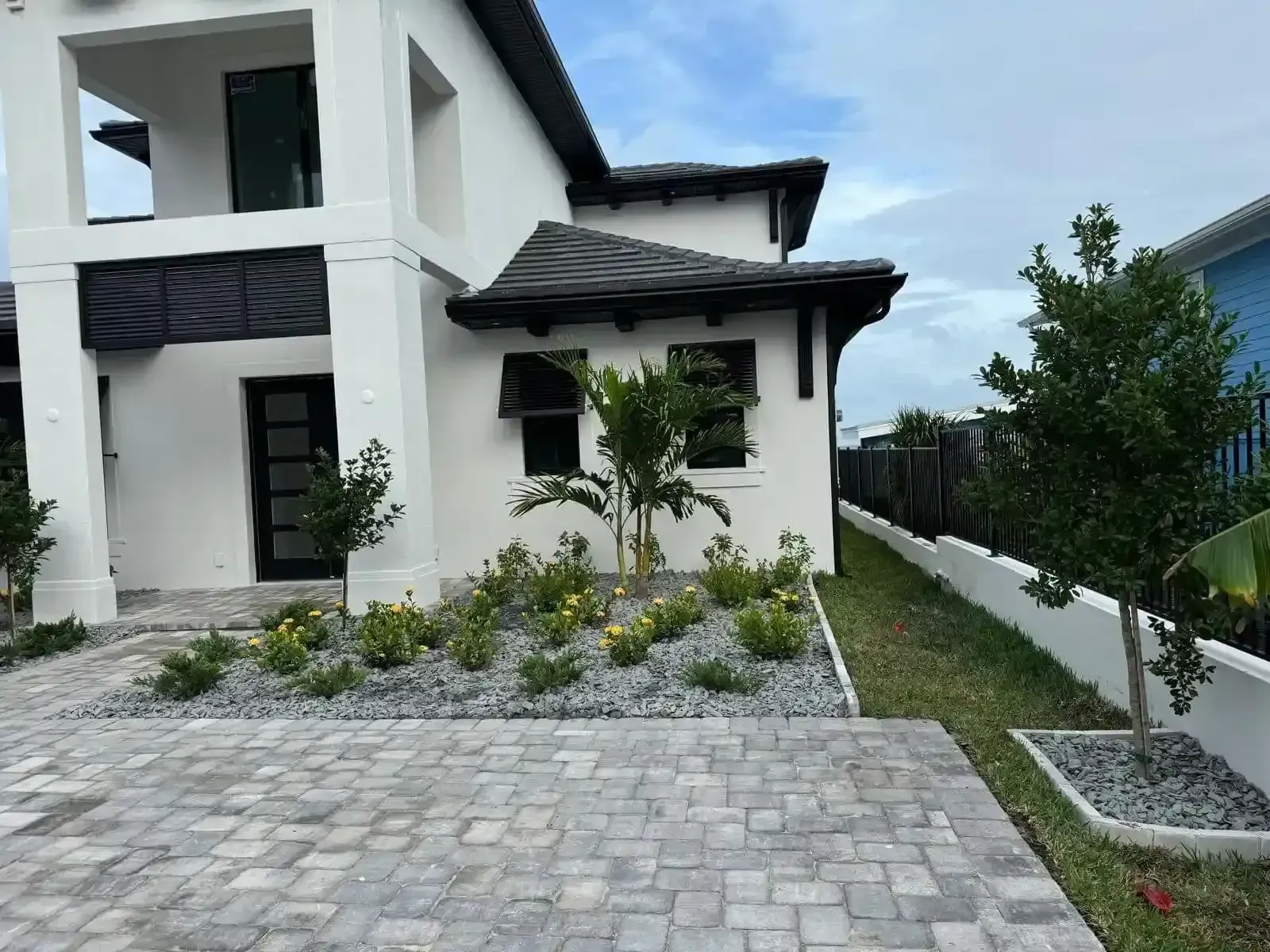 Modern white house with a dark roof and black shutters, featuring a grey stone garden bed and paved driveway.