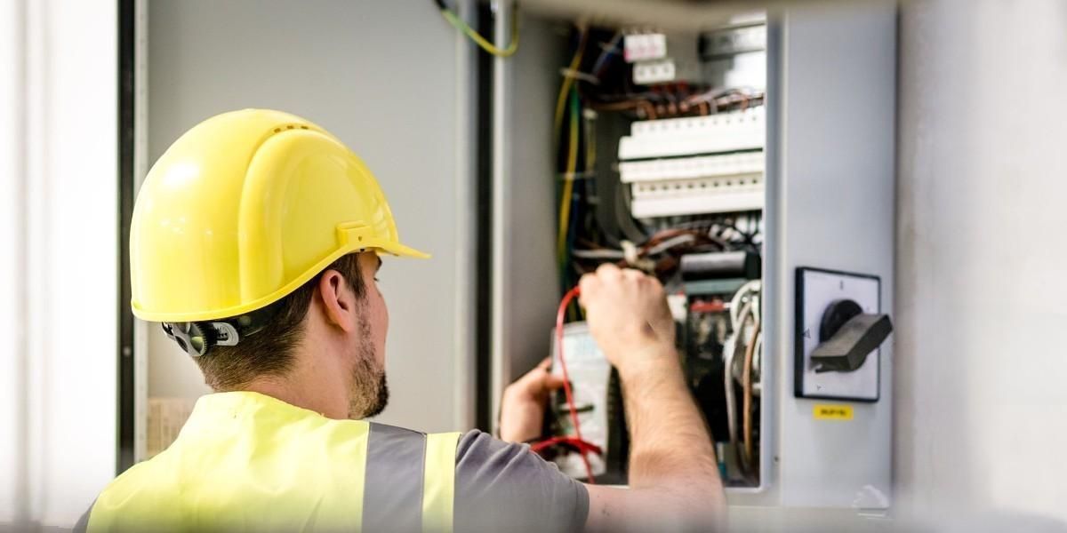 Electrician in yellow hardhat working on electrical panel.