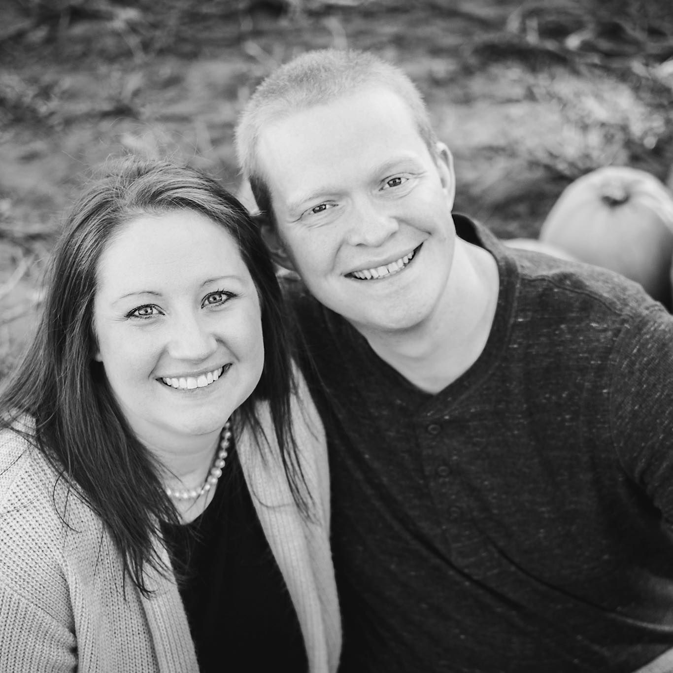 Smiling couple, woman with long hair, man with short hair, in front of pumpkins, black and white.