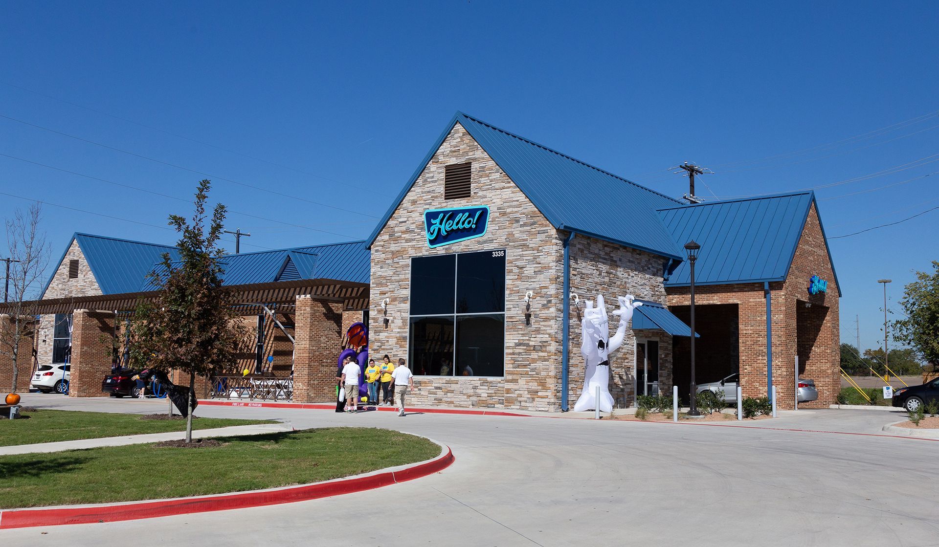 Outside of the Hello Deluxe Car Wash located in Garland, Texas featuring a stone building with blue roof, large window, and signage; exterior view under clear sky showing a car driving through the express car wash