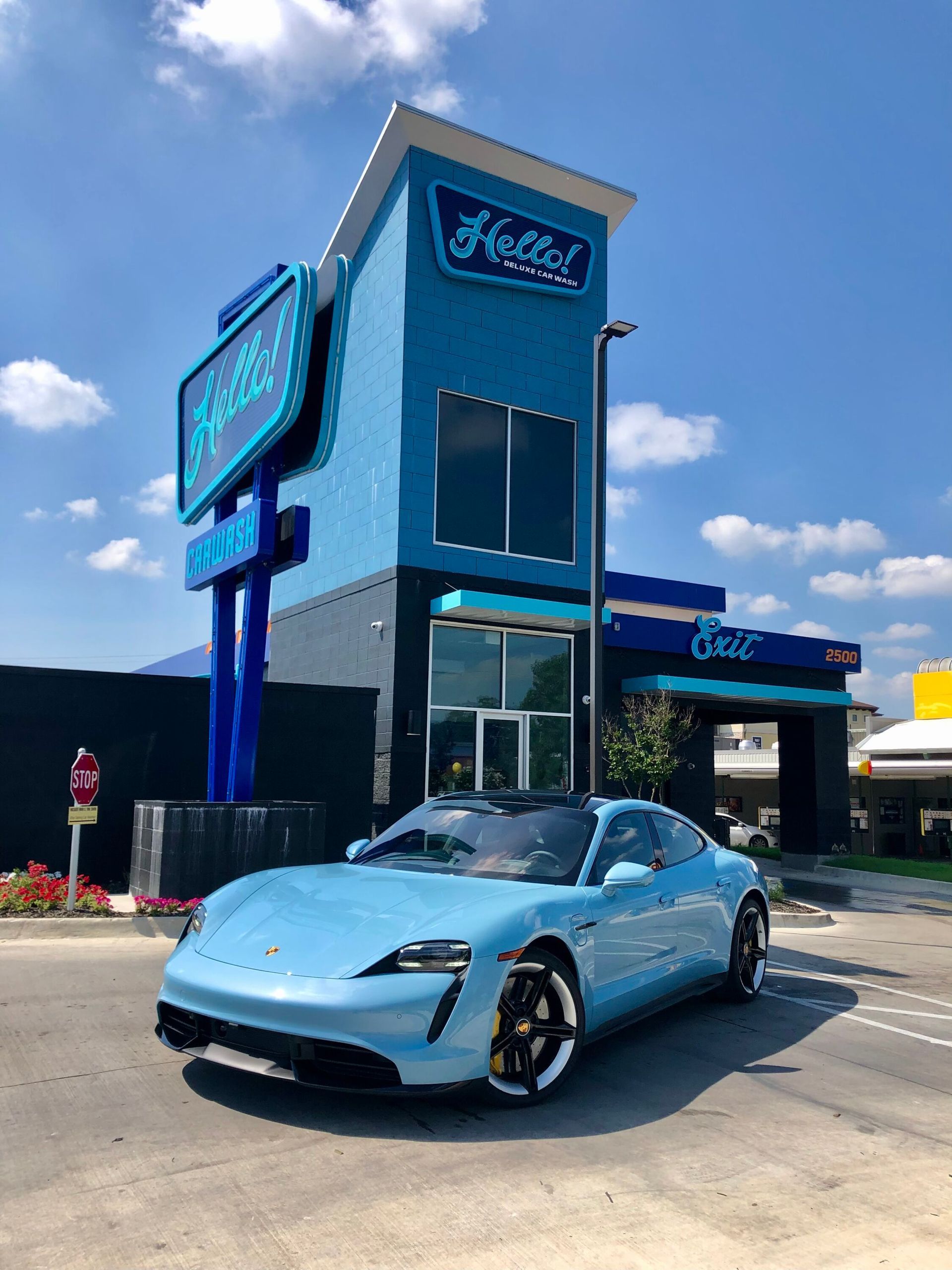 Light blue Porsche parked in front of the blue Hello Deluxe car wash building in the Kessler Park area of Dallas on a sunny day.