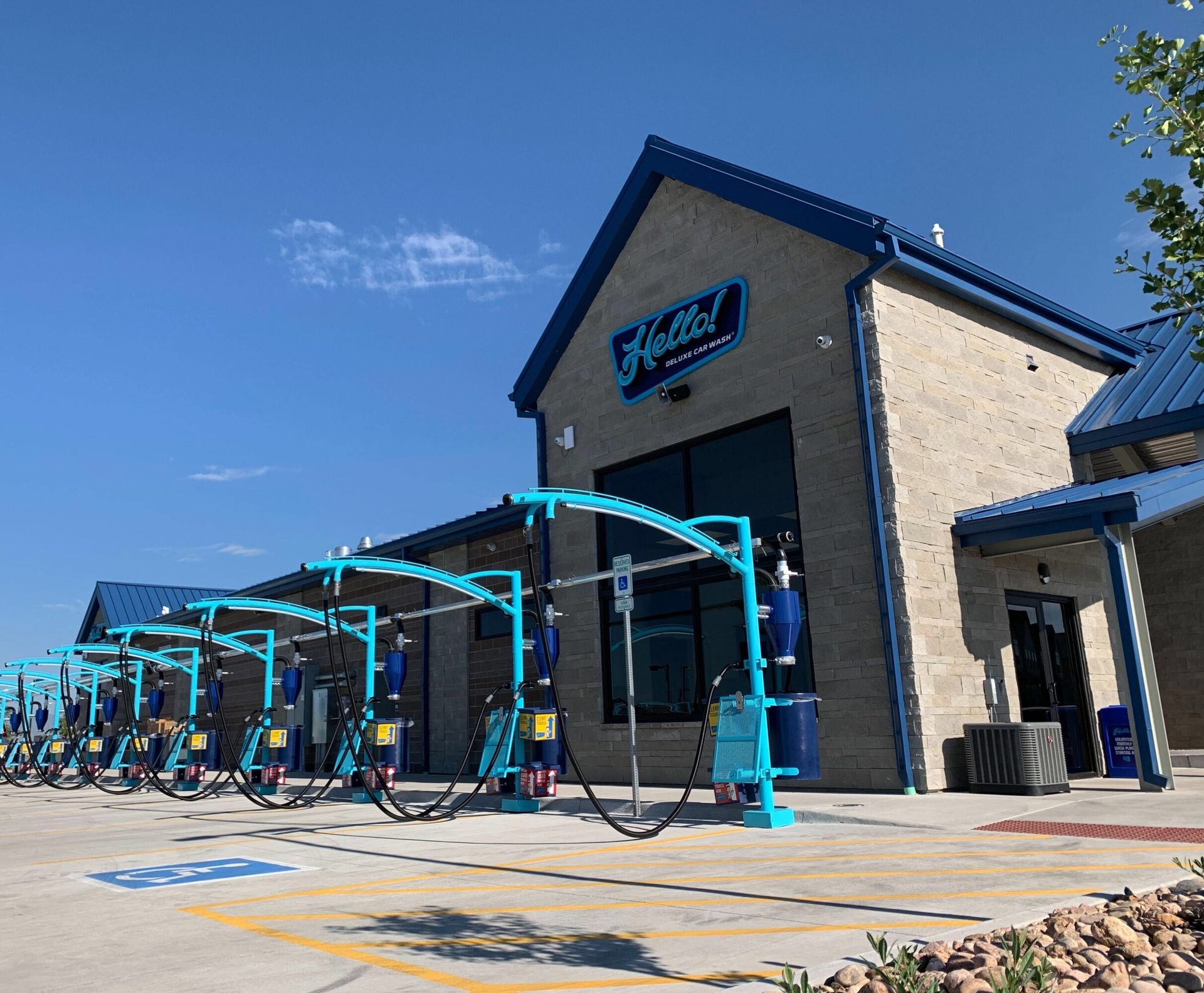 Exterior of the Hello Deluxe  drive through car wash facility on Central Park in Denver, Colorado with multiple bays and blue and teal accents. Clear blue sky.