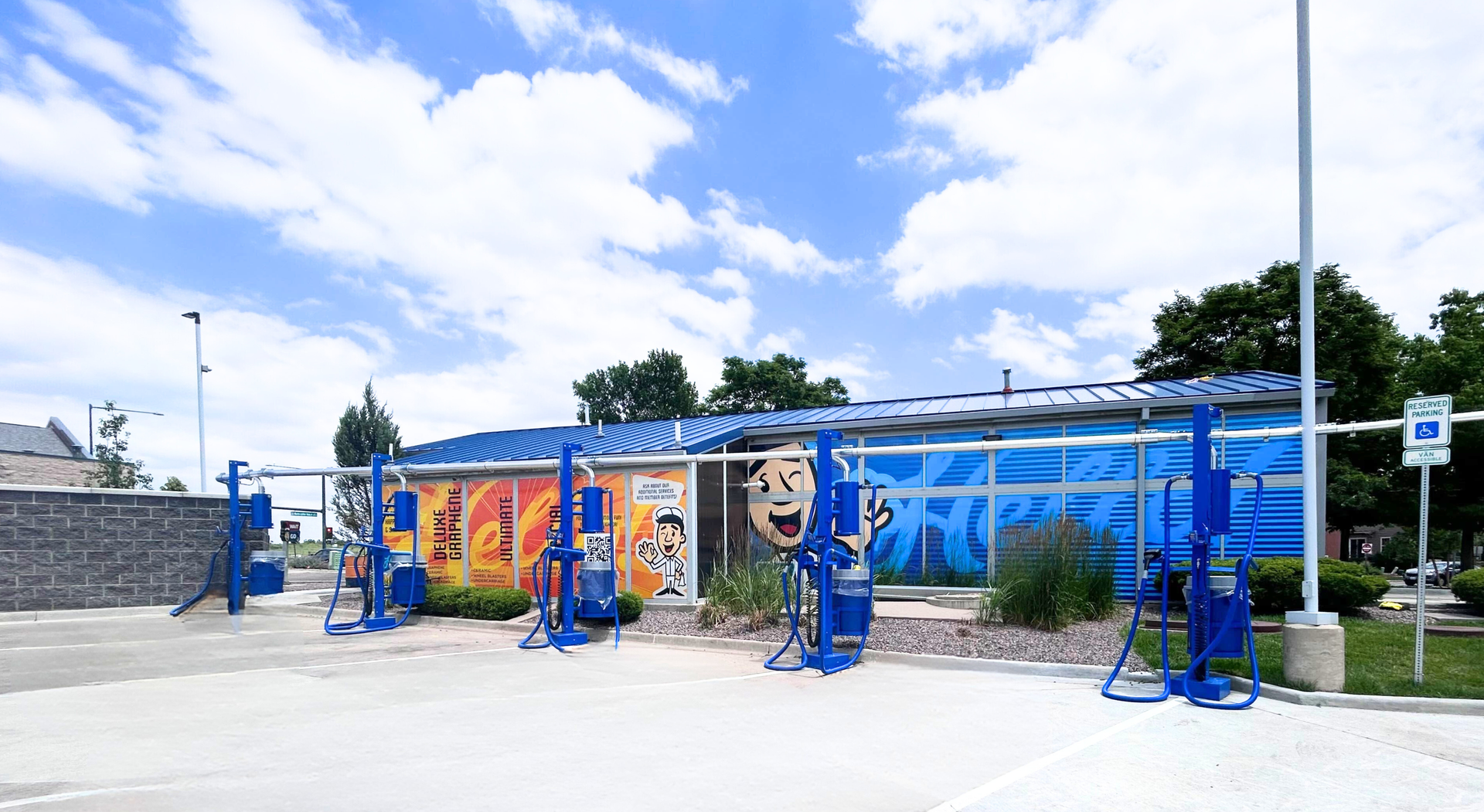 Exterior view of the Hello Deluxe Car Wash Eastbridge express wash located on  North, Iola Street in Denver, CO featuring a bright blue car wash with colorful art with 5 free vacuum stations off to the side
