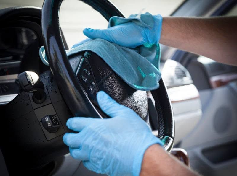 Hello Deluxe Car Wash employee polishing a blue car's headlight with a power tool, blue tape protecting surrounding paint.