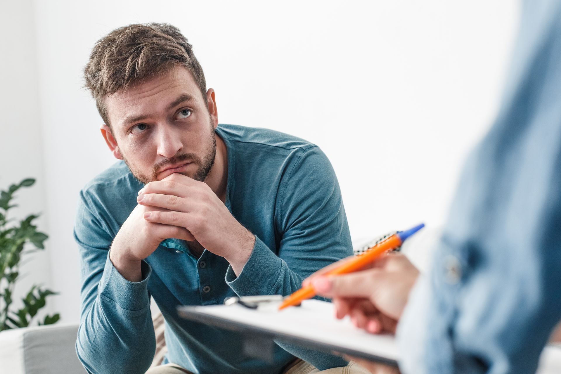 A man is sitting on a couch talking to a person holding a clipboard.