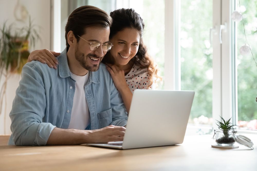 A man and a woman are sitting at a table looking at a laptop computer.