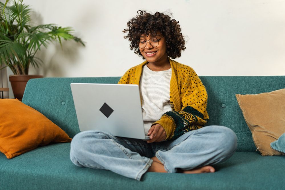 A woman is sitting on a couch using a laptop computer.