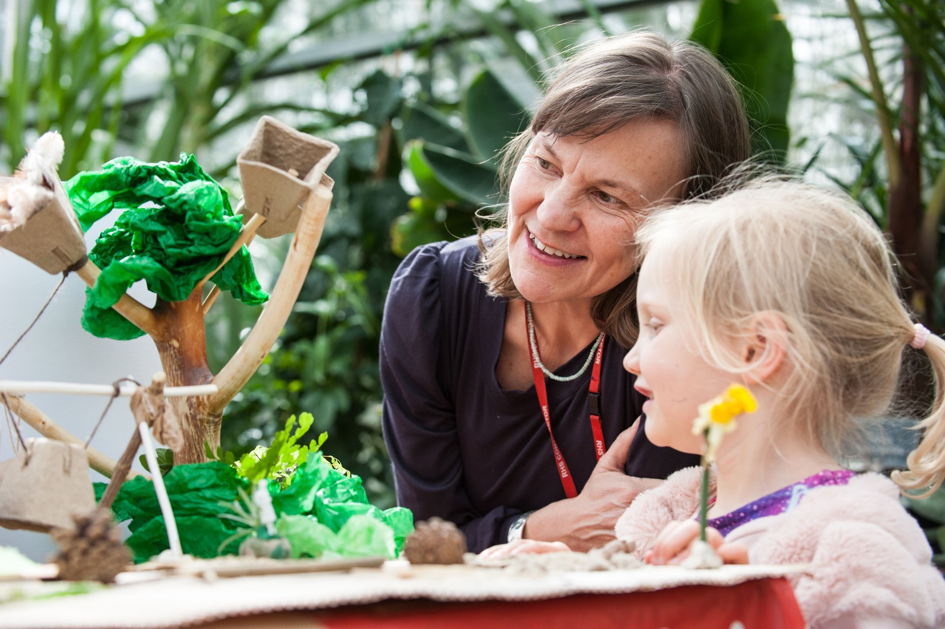 Woman and child examining a handmade tree and water feature. They are smiling in a greenhouse setting.