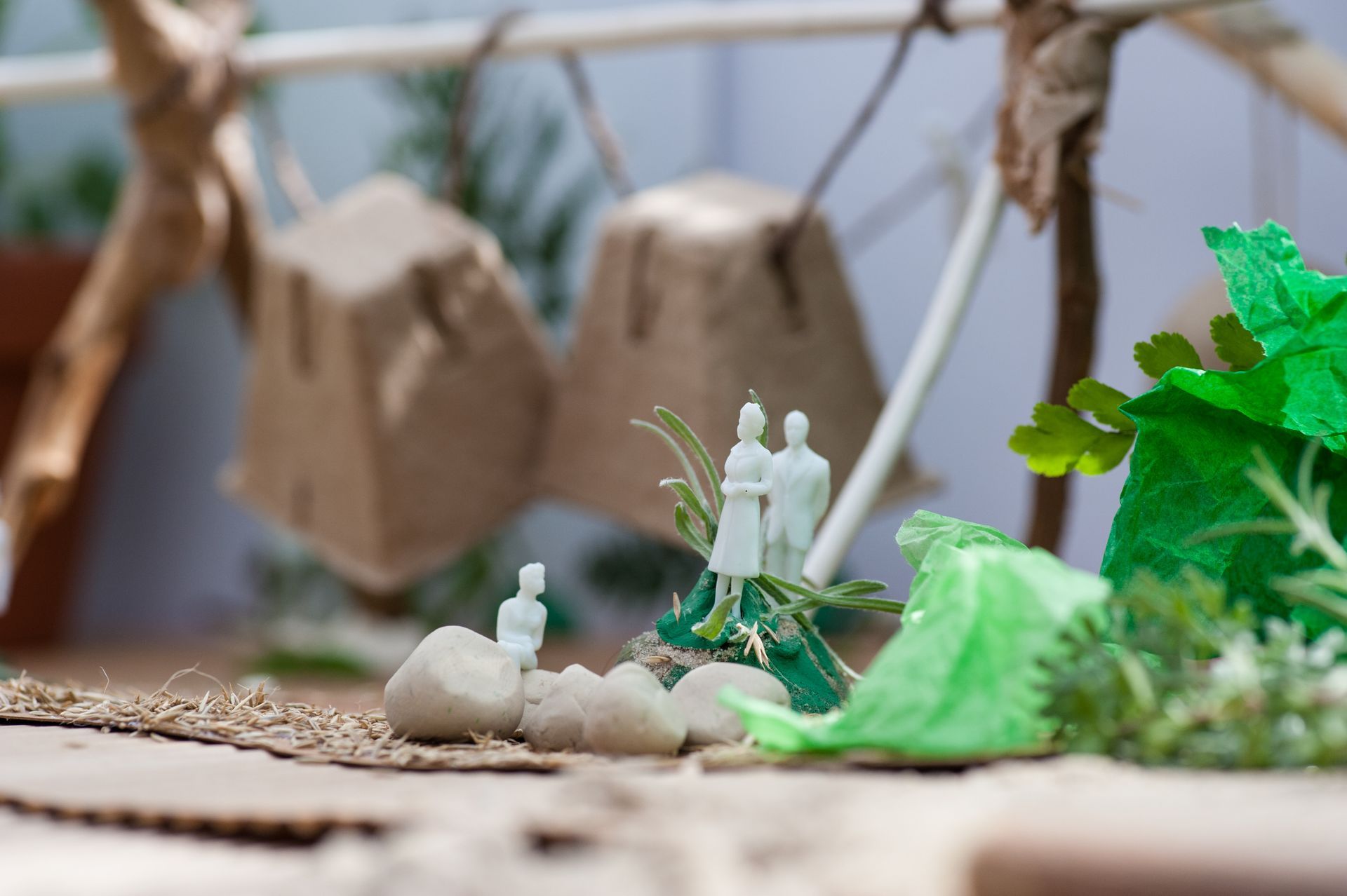 Miniature diorama with paper bag structures, tiny figures, green foliage, and natural materials.