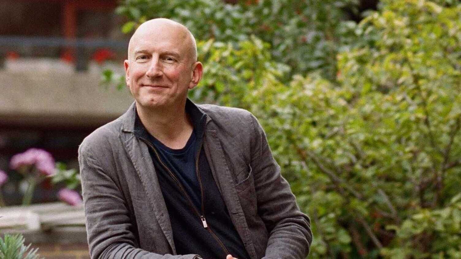 Smiling Nigel Dunnett in a gray jacket sitting outdoors in a garden-like setting