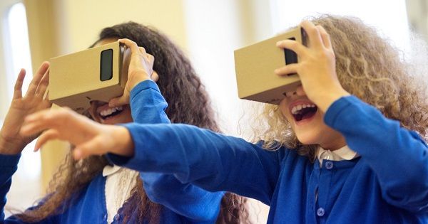 Two children wearing cardboard VR viewers, smiling, reaching, and appearing amazed.