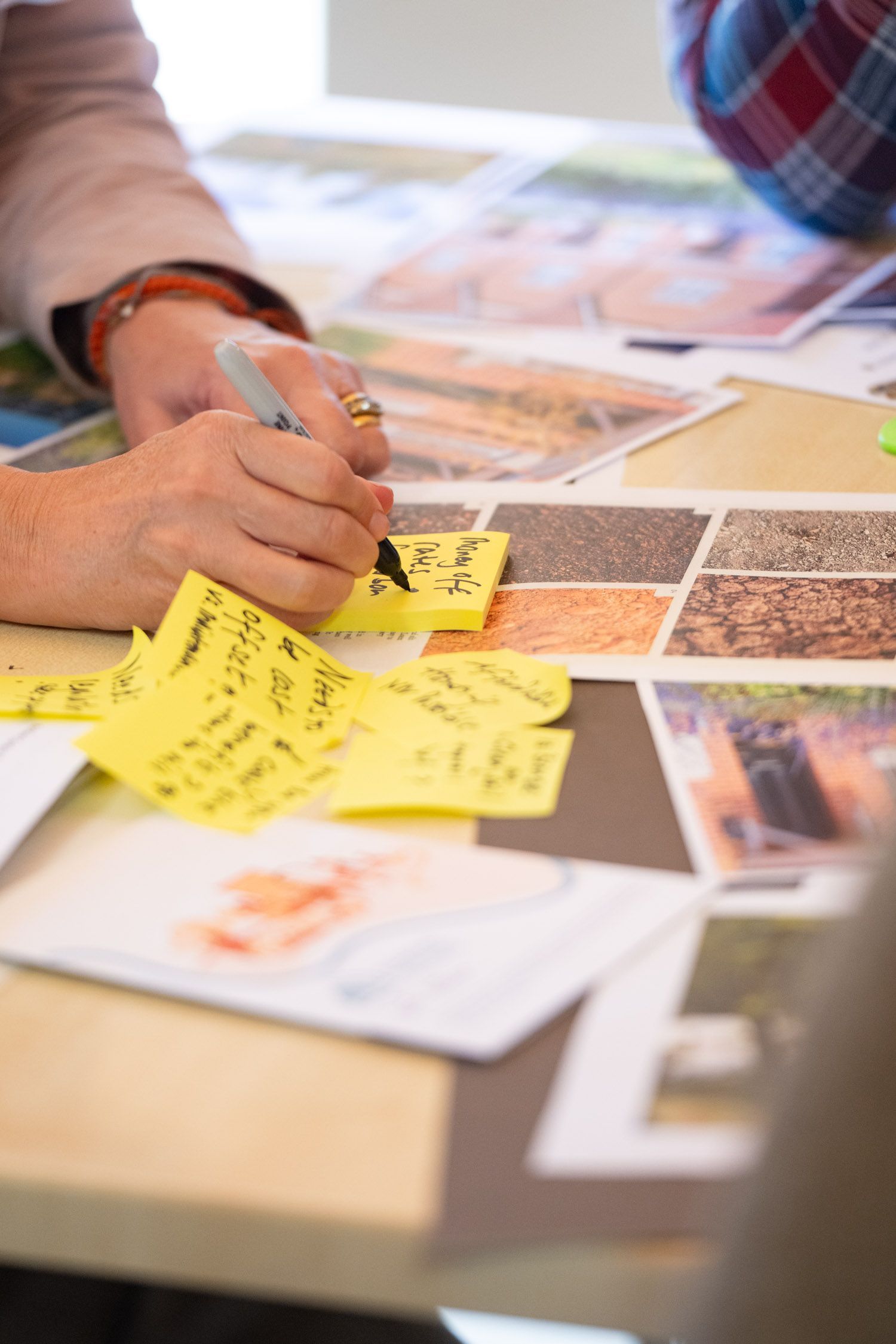 Person writes on yellow sticky notes laid on a table with images, possibly for a design project.