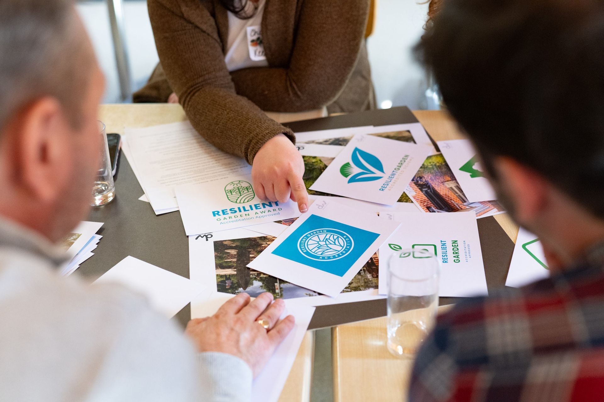 People examining designs at a table, one pointing to a blue logo, likely brainstorming.
