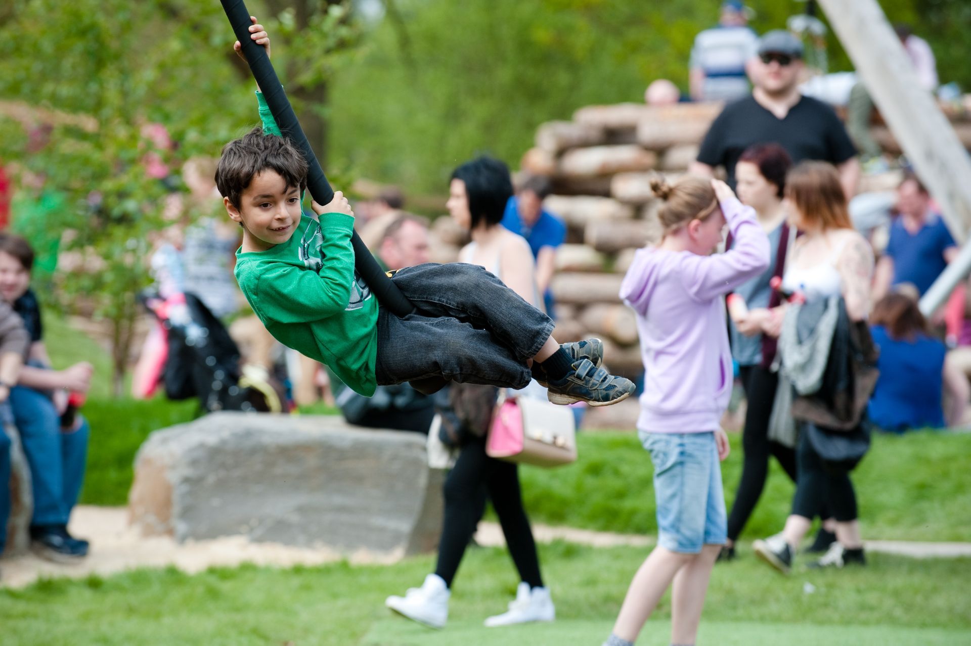 Boy swings on a rope in a park, smiling. People watch in the background.