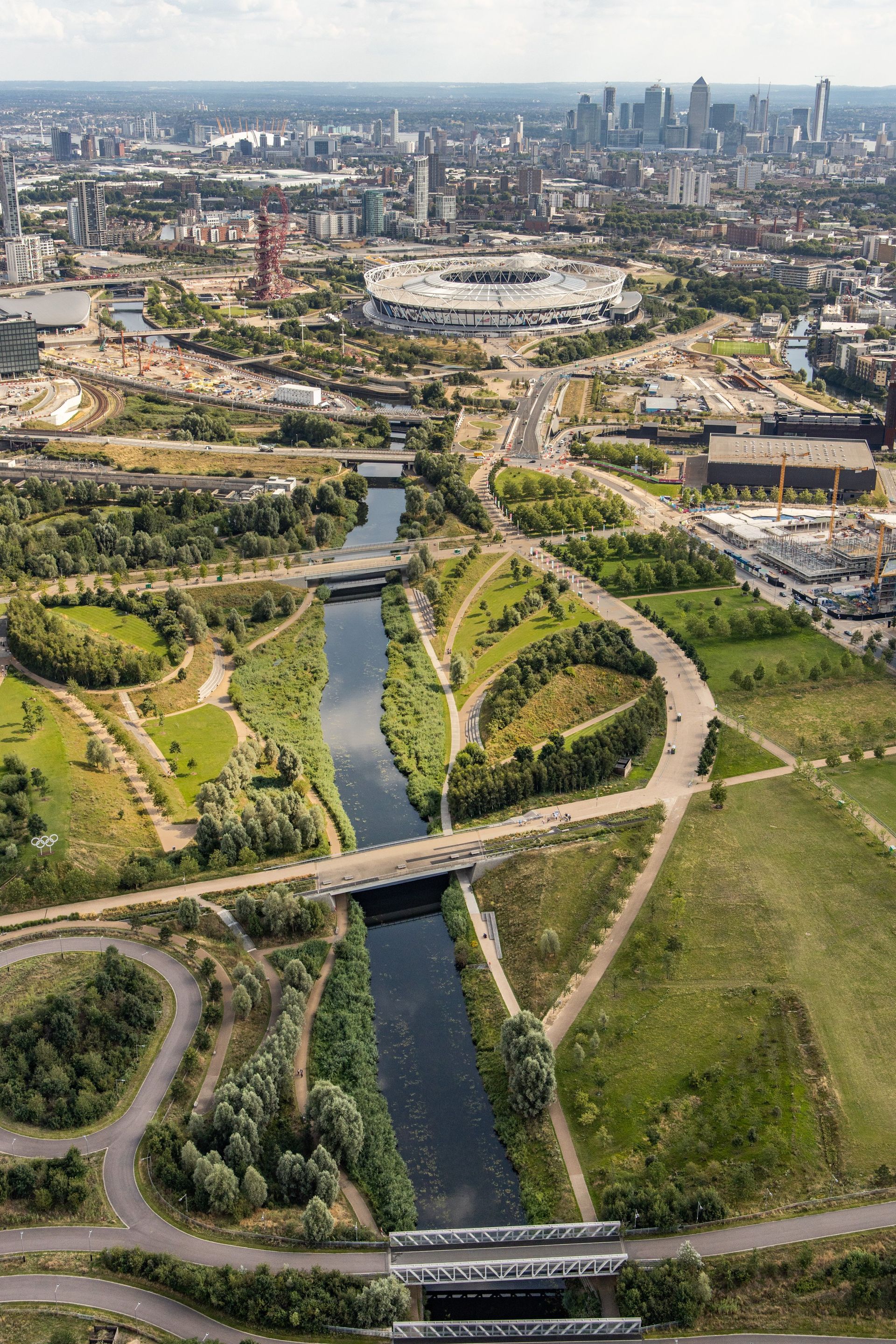 Aerial view of a river winding through green parkland and urban areas, with city skyline in the distance.