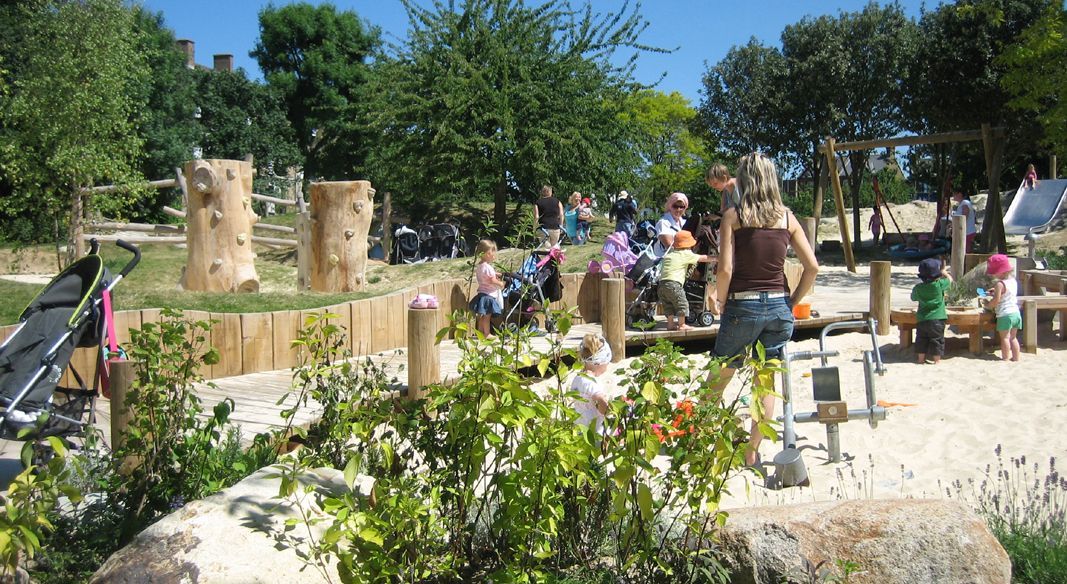 Playground with children climbing, playing, and parents supervising on a sunny day.