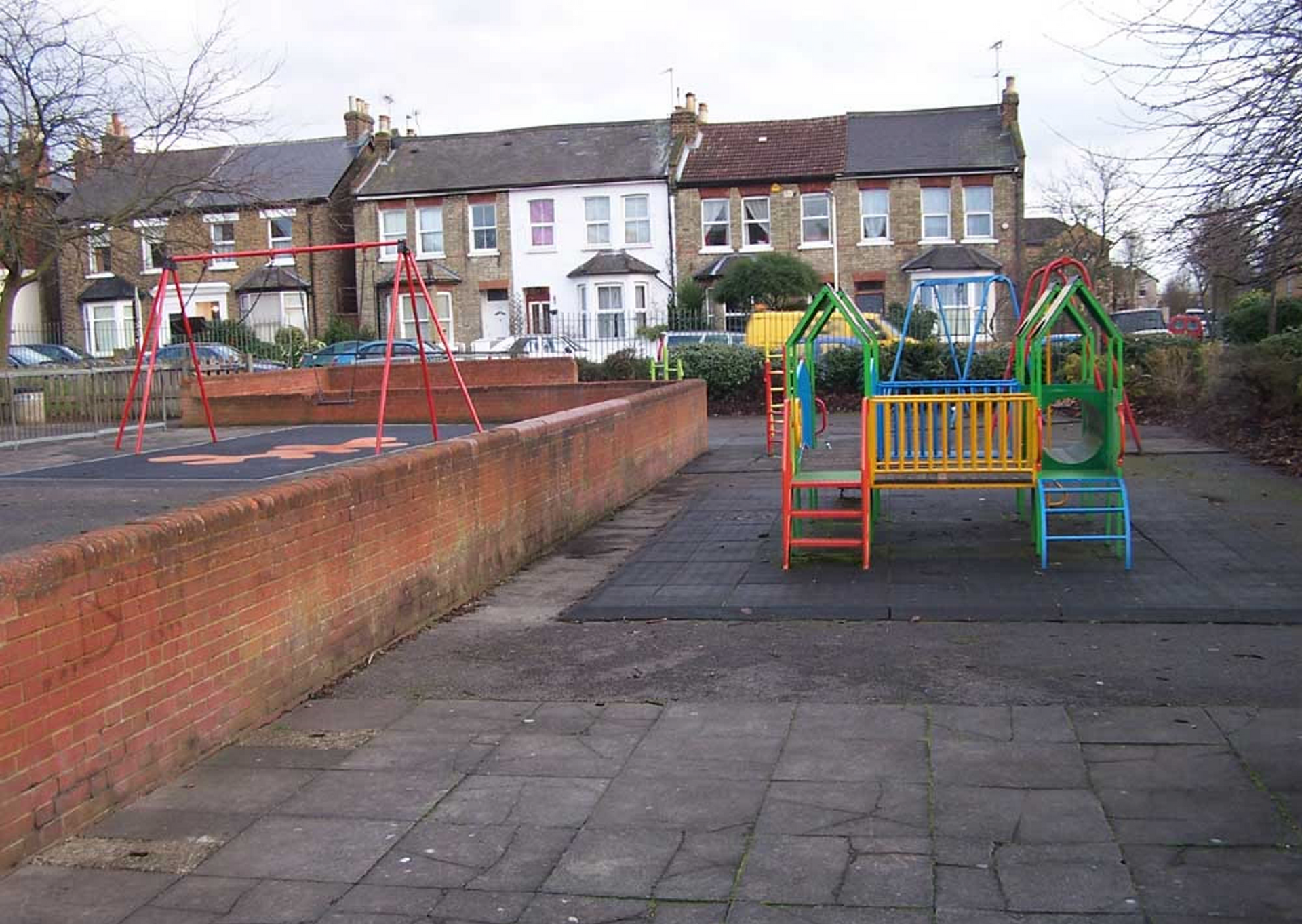 Playground with colorful equipment, brick wall, and row houses in the background.