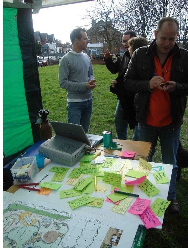People at an outdoor table with sticky notes and a projector; a man on the right is using his phone.