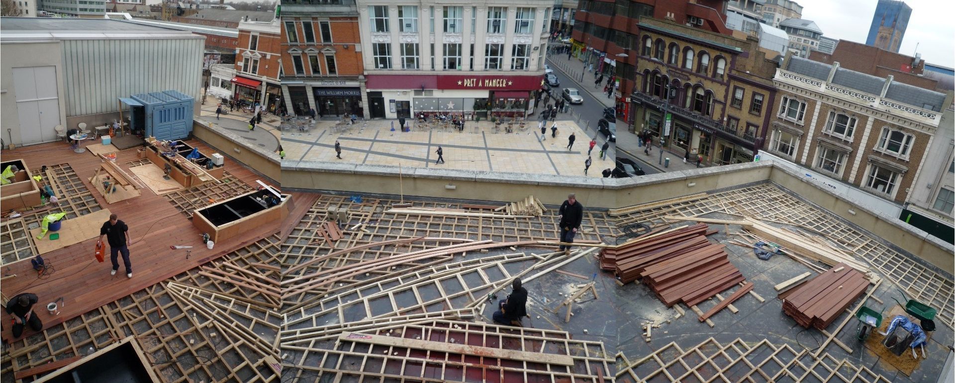 Workers installing tiles on a roof overlooking a city square with shops and buildings.