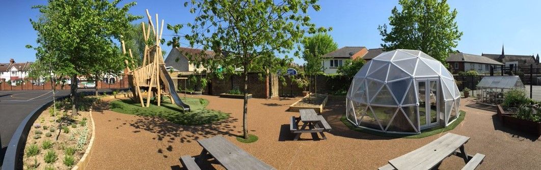 A playground with wooden structures, a geodesic dome, picnic tables, and a blue sky.
