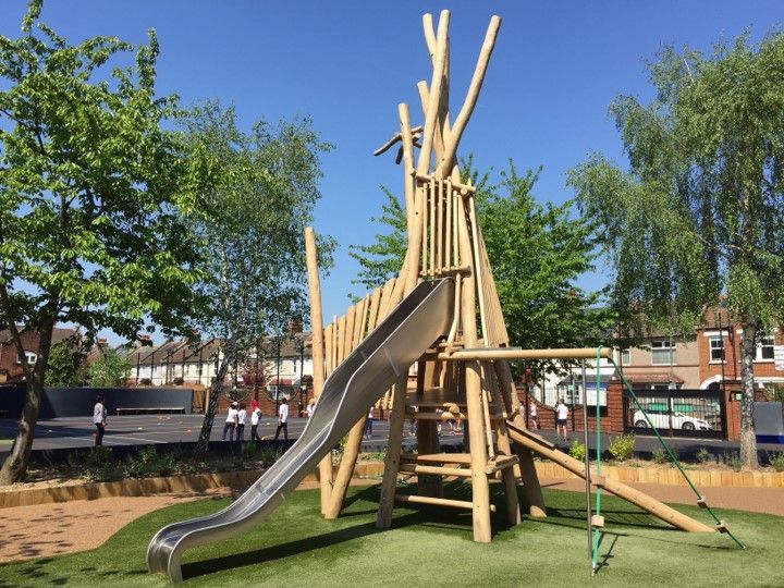 Wooden playground structure with slide, climbing elements, and green turf, in a sunny park setting.