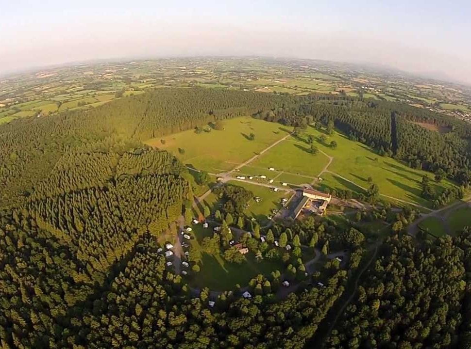 Aerial view of a campground nestled in a forest clearing with a meadow, surrounded by dense green trees.