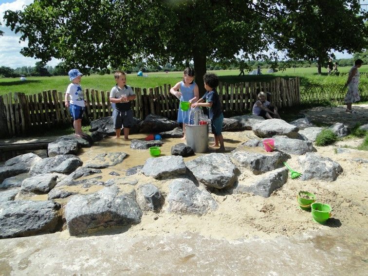 Children playing with water and sand in a park, under a tree.