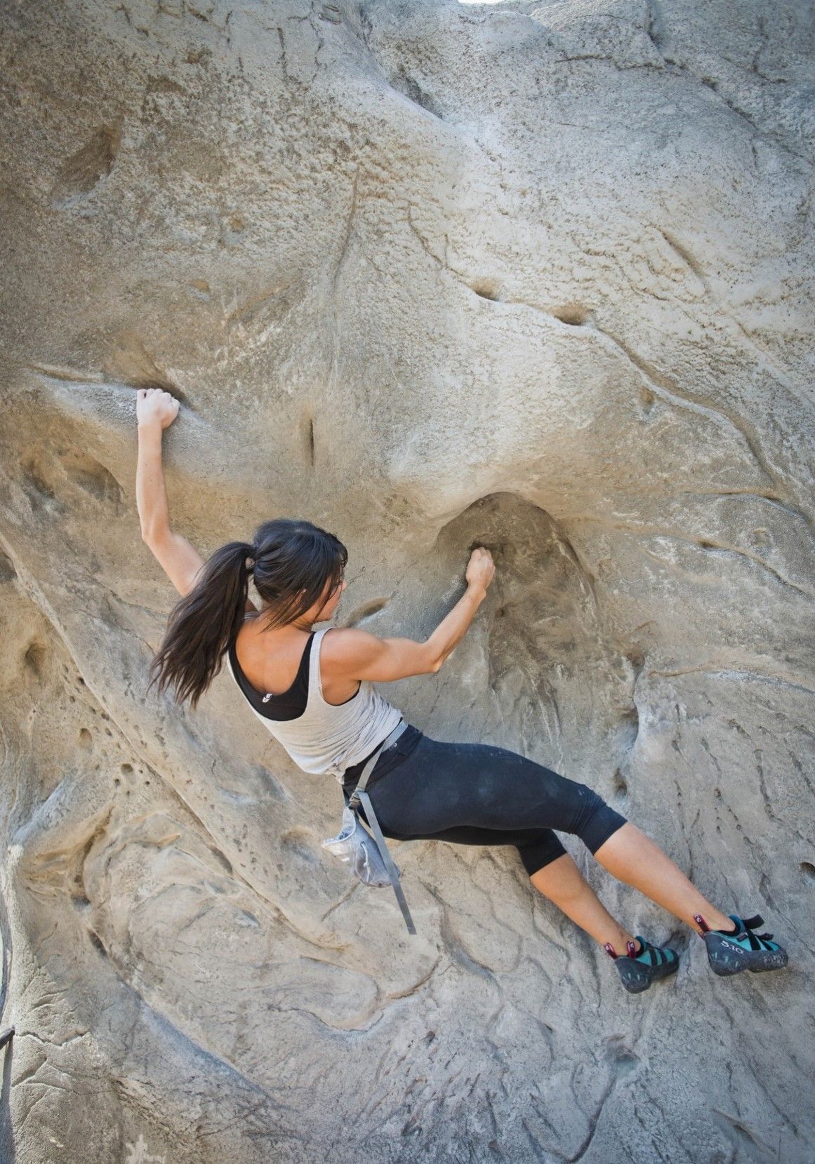 Woman rock climbing on a gray rock face, reaching for a hold with a focused expression.