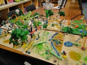 A child's colorful, mixed media diorama on a tabletop, depicting a whimsical landscape with trees, roads, and structures.