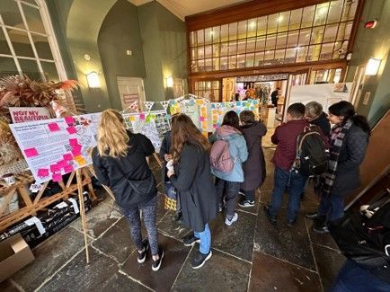People viewing posters and documents, possibly at a public display, inside a building with glass doors.