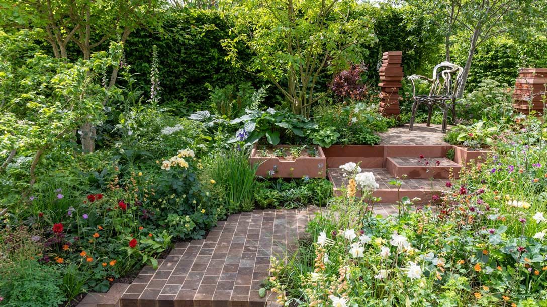 Lush garden with brick path, flowering plants, and brick steps leading to a small patio area