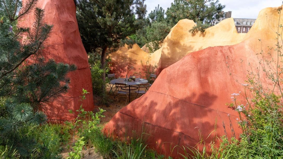 Project Giving Back Garden - Red and yellow sculpted rock formations among trees and shrubs in a landscaped outdoor setting