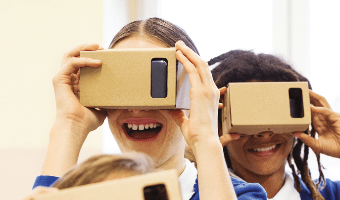 Three smiling students wearing cardboard VR viewers indoors.