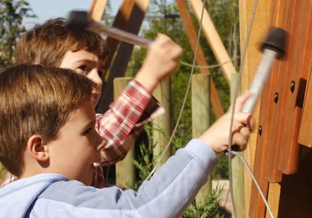 Two boys playing a wooden outdoor musical instrument, striking it with mallets.
