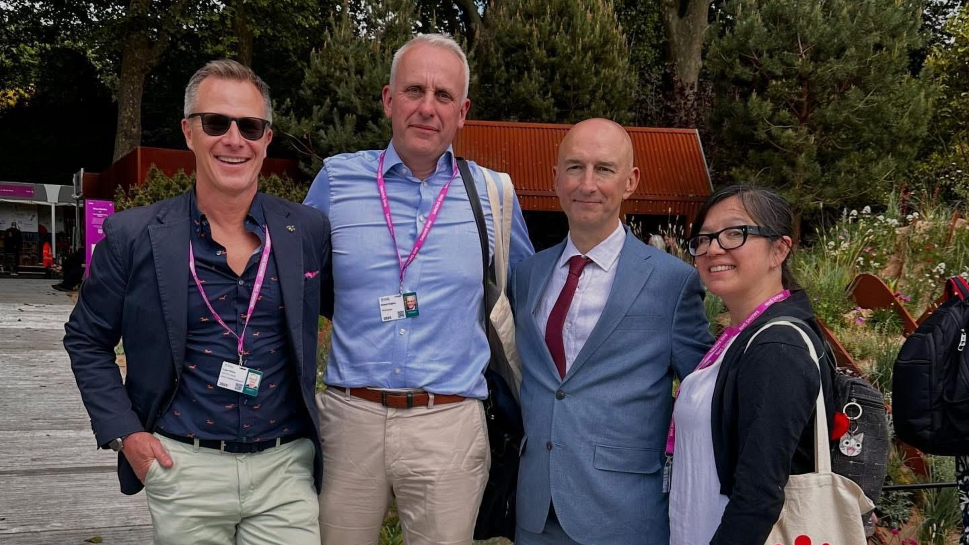 AdamWhite and 3 people posing outdoors at an event, wearing badges and formal-casual clothes.