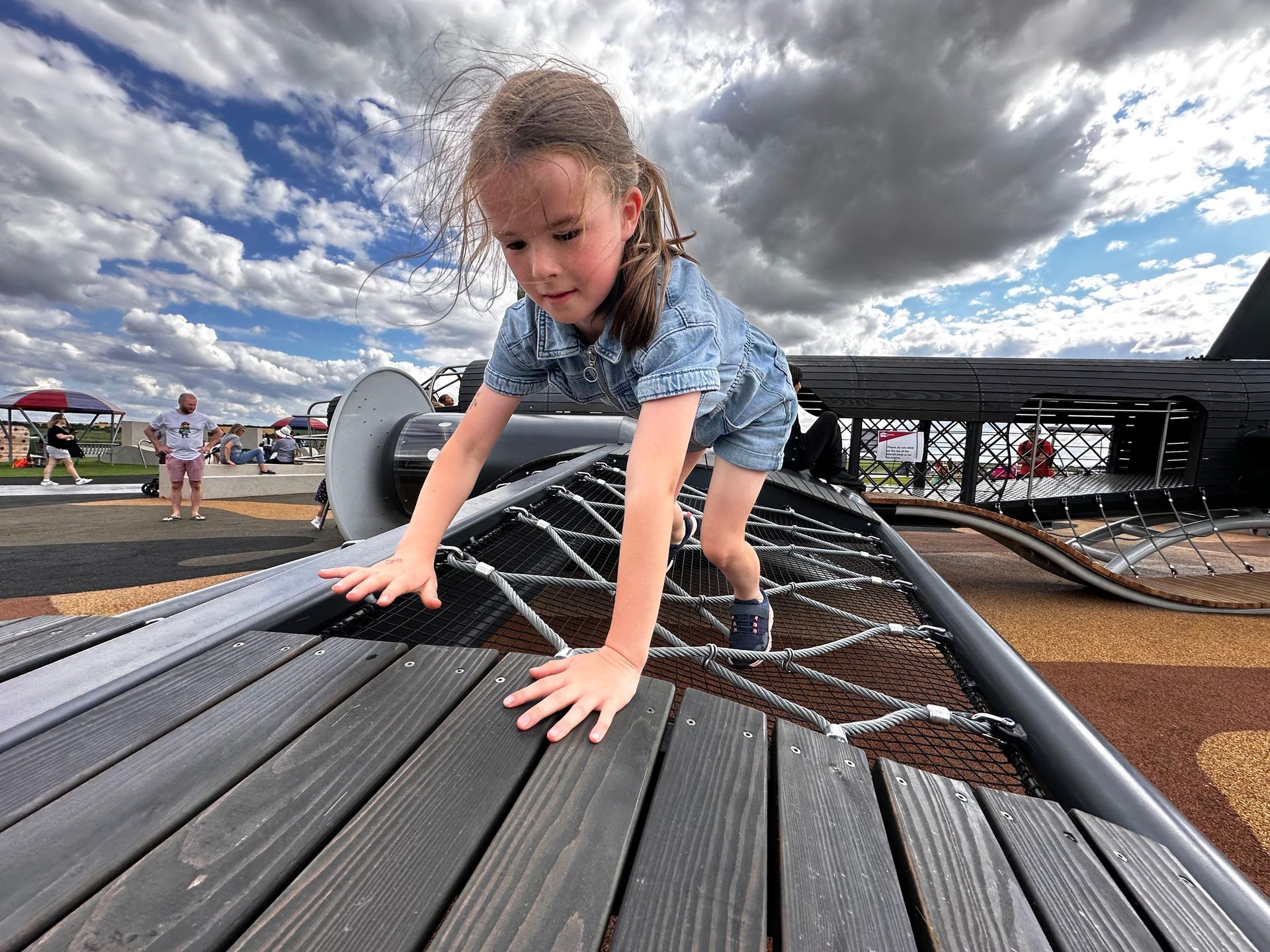 Girl climbs a rope net on playground. Overcast sky.