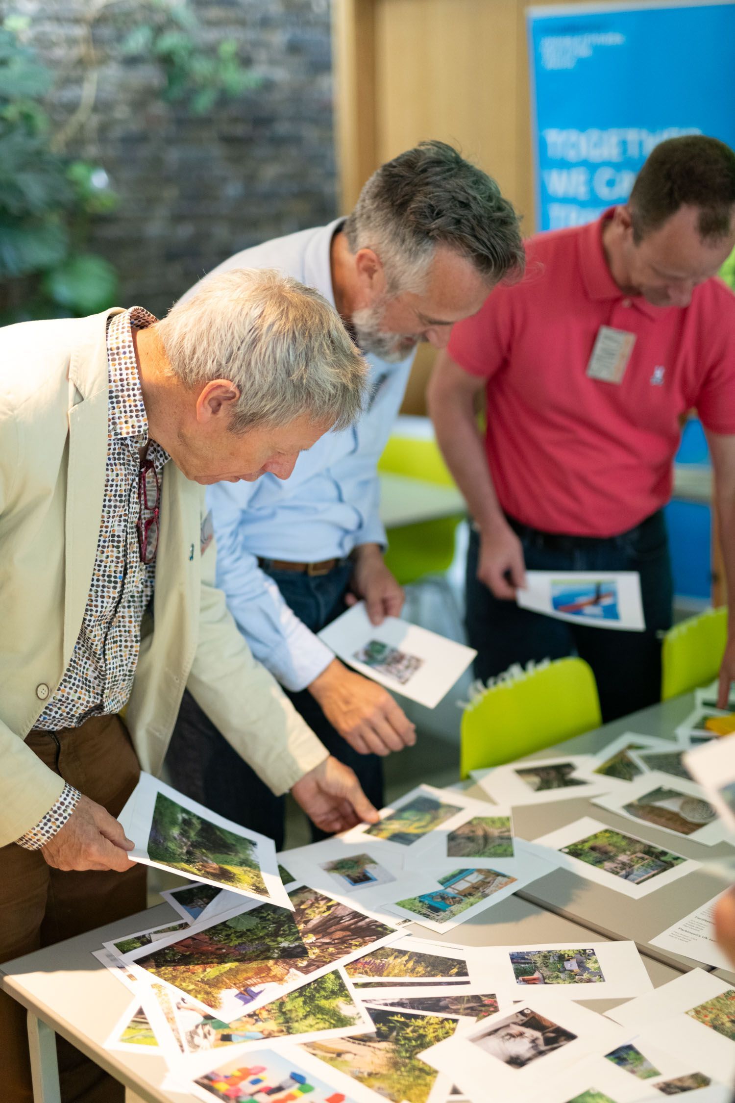 Three people reviewing printed photos spread across a table at an indoor event booth