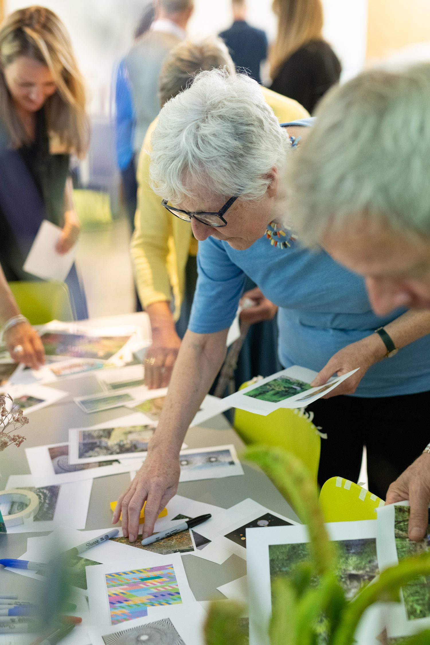 People leaning over a table, examining colorful printed materials and papers at an indoor event