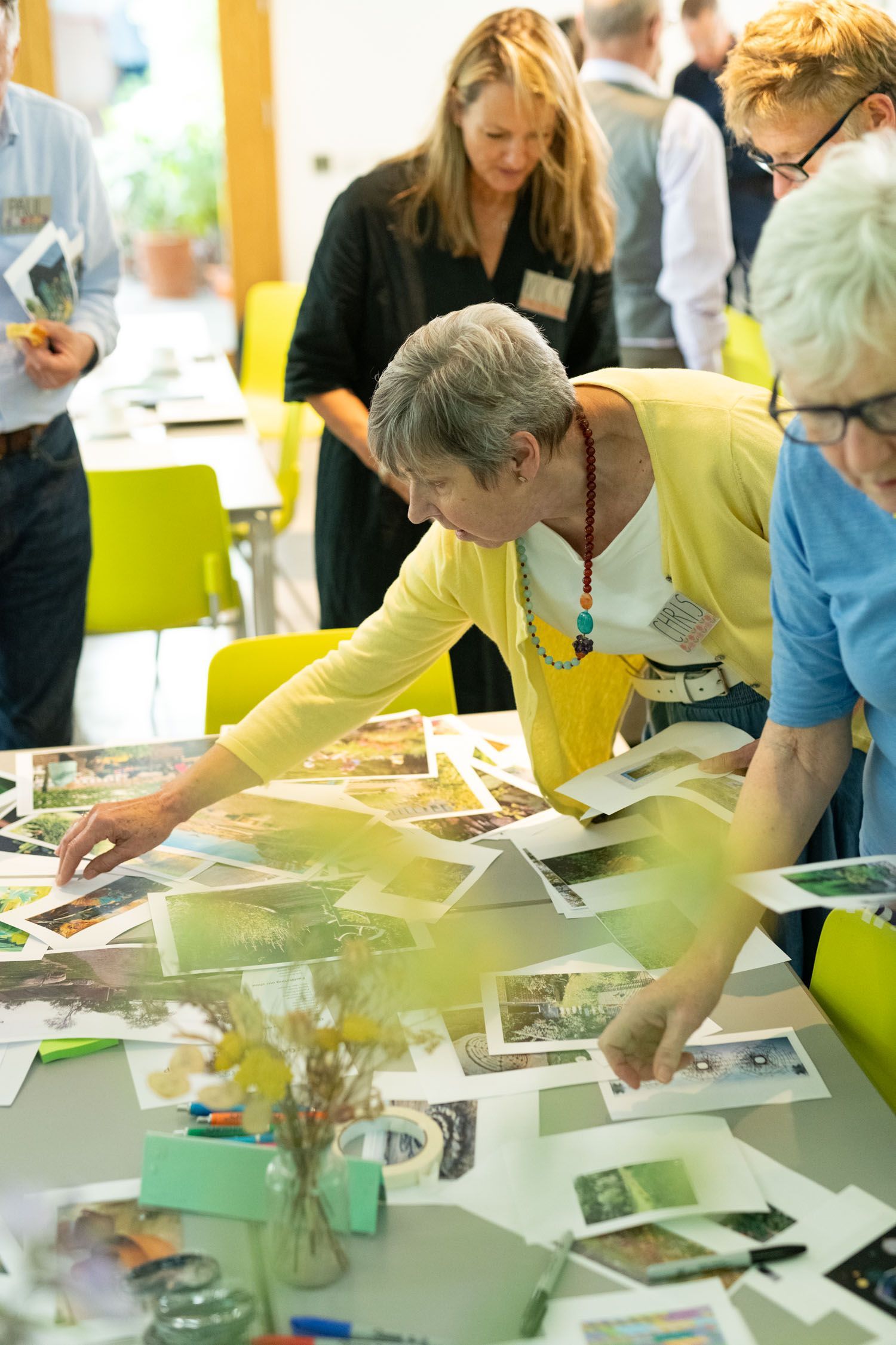 People leaning over a table, sorting and pointing at printed photos and papers in a bright workshop space